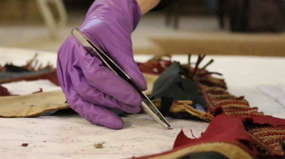 Image of Gloved hand holding tweezers for the conservation of a textile banner
