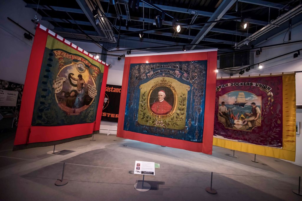 Image of Three big colourful textile banners hanging in a large gallery space.