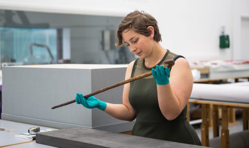 Image of Collections Officer Sam Jenkins with Peterloo cane from around 1819, in The Conservation Studio at People's History Museum, Manchester