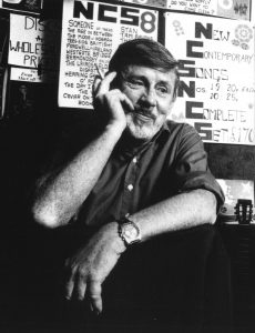 Black and white photograph of a white male, Ewan MacColl, with a cigarette in one hand.