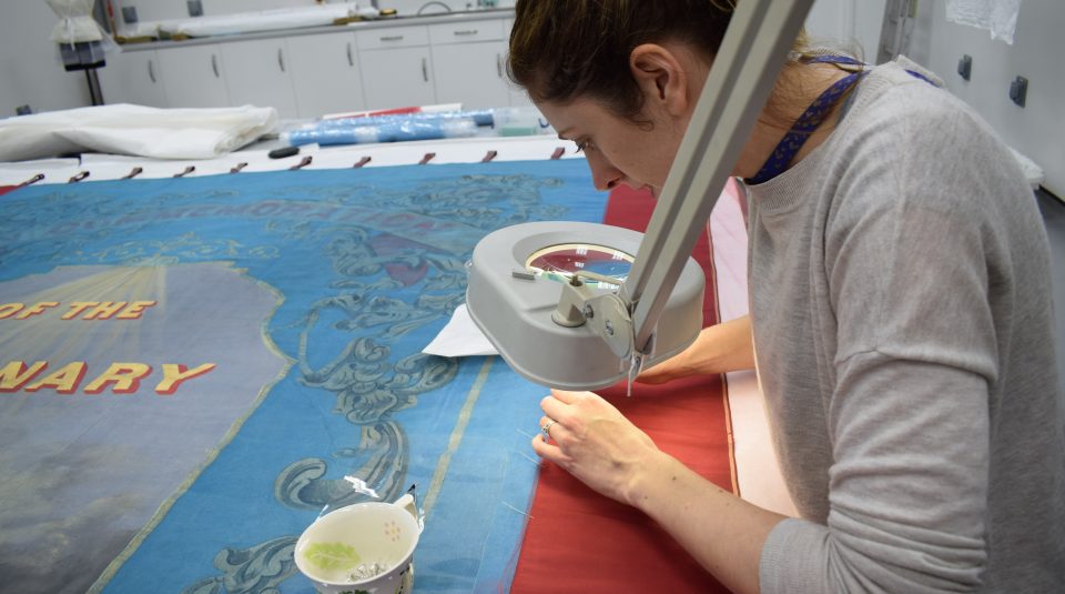 Image of Jenny van Enckevort stitching the net to the borders on the Downham Benevolent Society banner