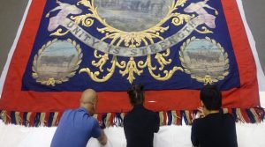 Three people kneeling with a large red and blue fringed banner