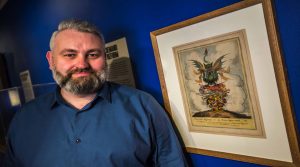 Mark Wilson, Exhibitions Officer with Universal Suffrage or the Scum Uppermost hand coloured engraving in Disrupt? Peterloo and Protest exhibition