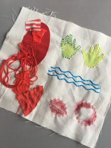 Image shows a textile piece on white fabric, symbols of hands, water and lips have been stitched using various stitching techniques. 