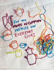 Image shows textile piece on a white fabric with colourful stitching. The words 'For me More in Common reflects our everyday lives' has been stitched in blue and pink thread. Around the letters are images of kettles and tea pots also in multi-coloured stitching. 