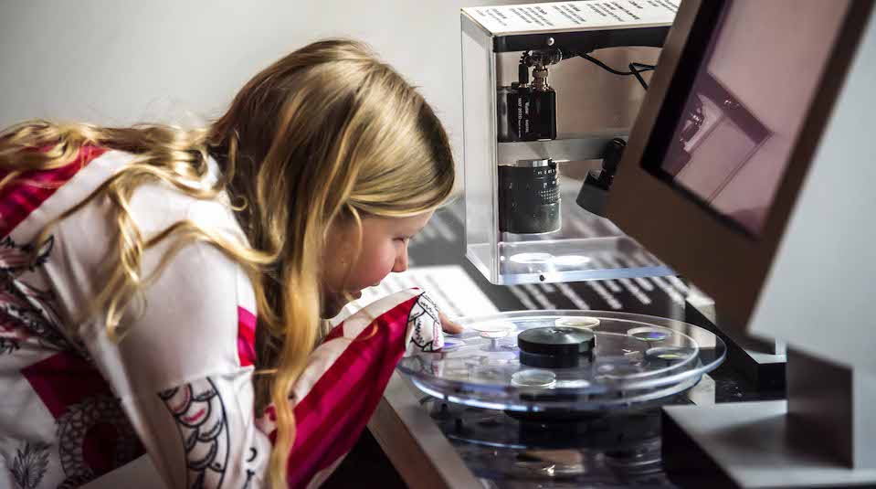 Image of Visitor using a microscope at the Conservation Studio viewing window in Main Gallery Two at People's History Museum