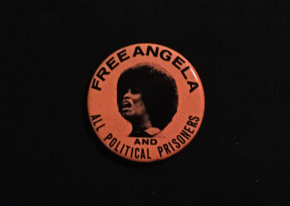 An orange and black badge with a photograph of a face on it.