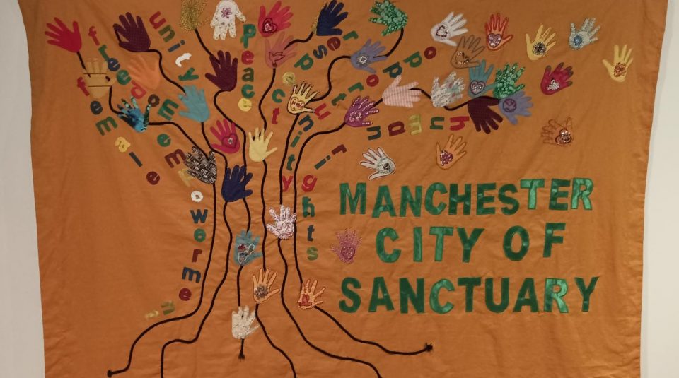 Image of Colourful banner with the words 'Manchester City of Sanctuary' sewn on in green material.
