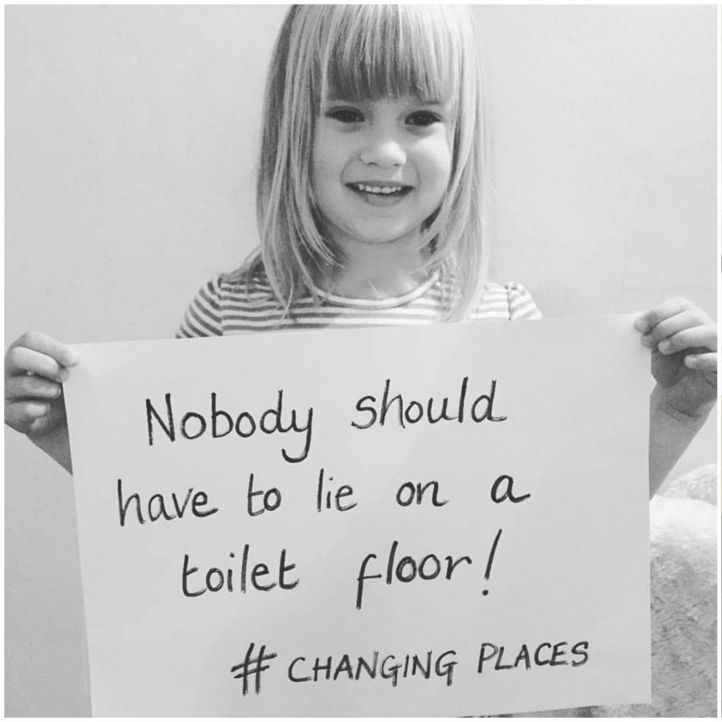 Image of child holding a sign with text ‘Nobody should have to lie on a toilet floor!’ for Changing Places toilet campaign. Image courtesy of changing-places.org.