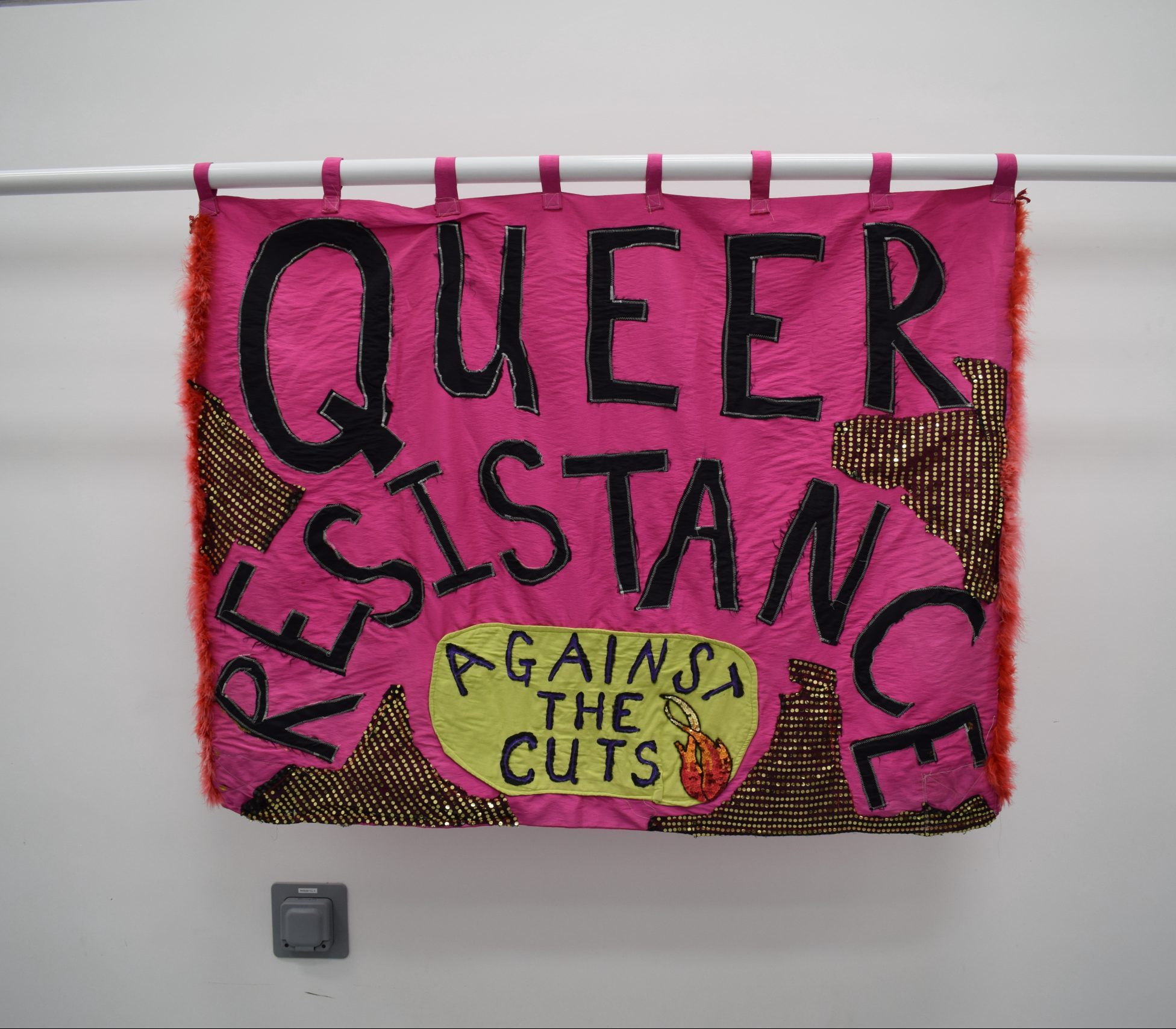 A pink banner which says Queer Resistance Against the Cuts. 