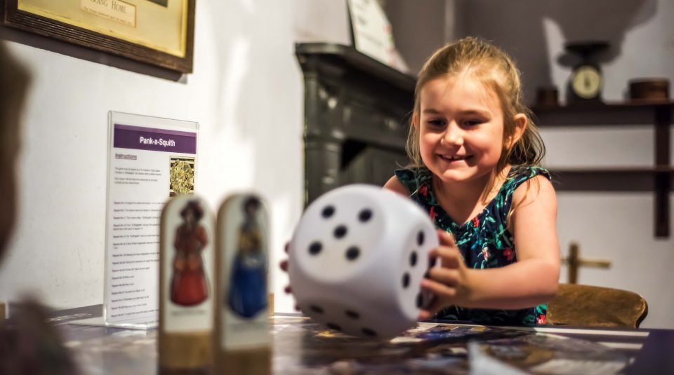 Image of visitor playing the Pank-a-Squith board game in suffragette Hannah Mitchell's kitchen in the Voters section of Main Gallery One at People's History Museum.