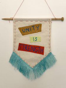 Mini textile banner with stitched words ‘Unity and Strength’, White cotton background with turquoise tassel