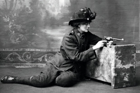 Image of Constance Markievicz in uniform, kneeling against a studio prop holding a gun.