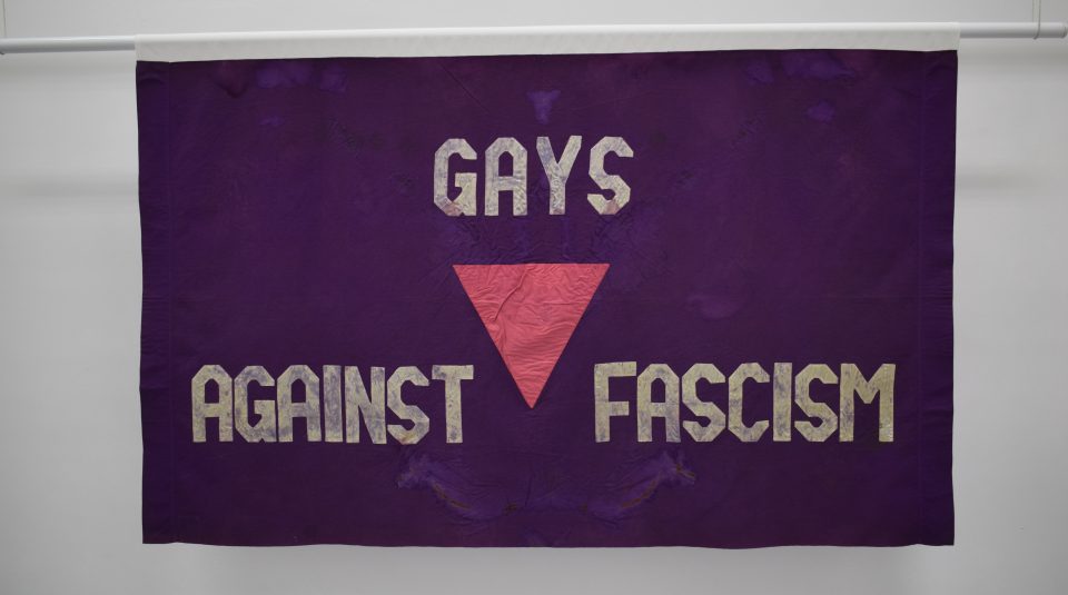 Image of A purple banner with a pink triangle that says 'Gays Against Fascism'.