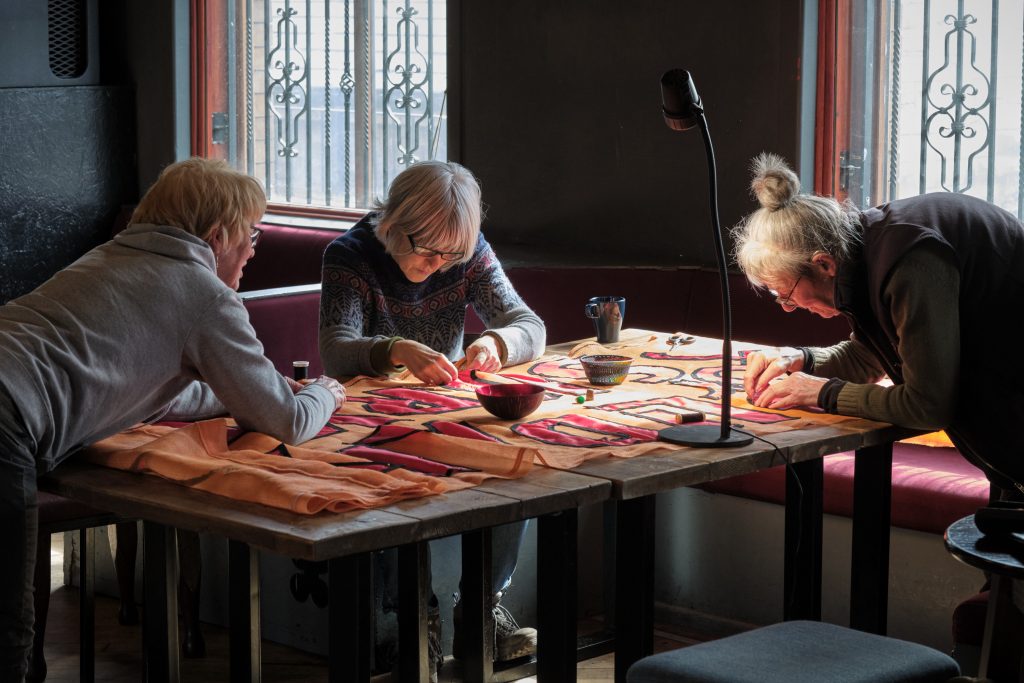 Three people around a table sewing an orange banner.
