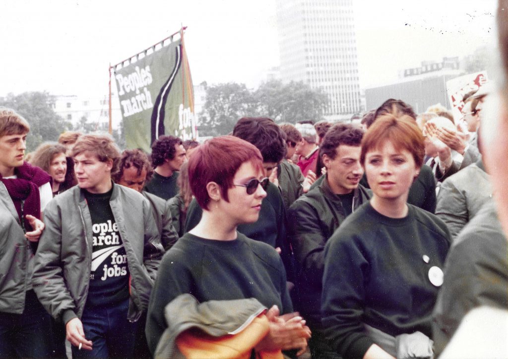 Colour photograph of people marching in a protest. There is a banner with the text People’s march for jobs.