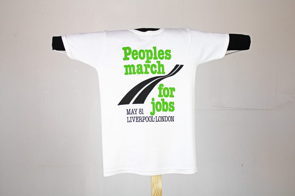 Image of White t-shirt with green text and a black road. The text reads: 'Peoples march for jobs MAY 81 LIVERPOOL-LONDON'.