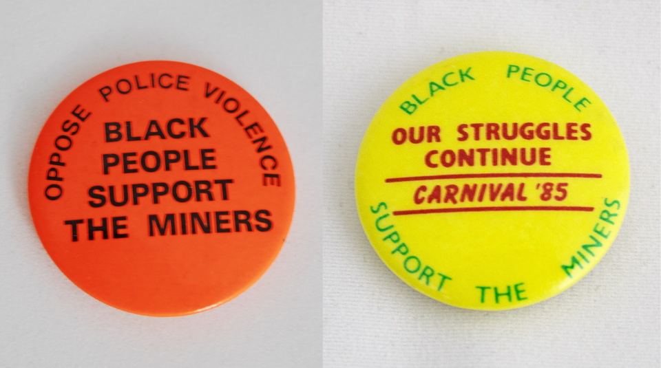 Image of Left to right: An orange badge which says 'Oppose police violence black people support the miners'. A yellow bade which says 'Black people support the miners our struggles continue Carnival '85.'