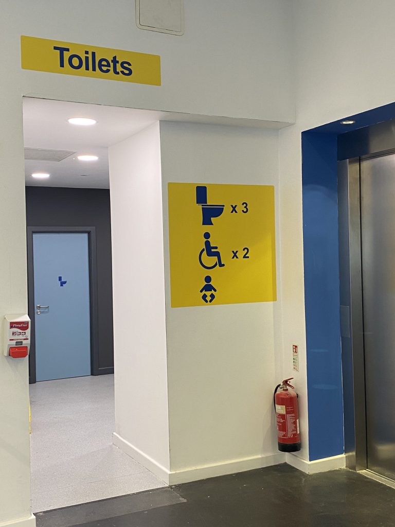 entrance doorway with a sign above with dark blue text on a yellow background reading: 'Toilets'.