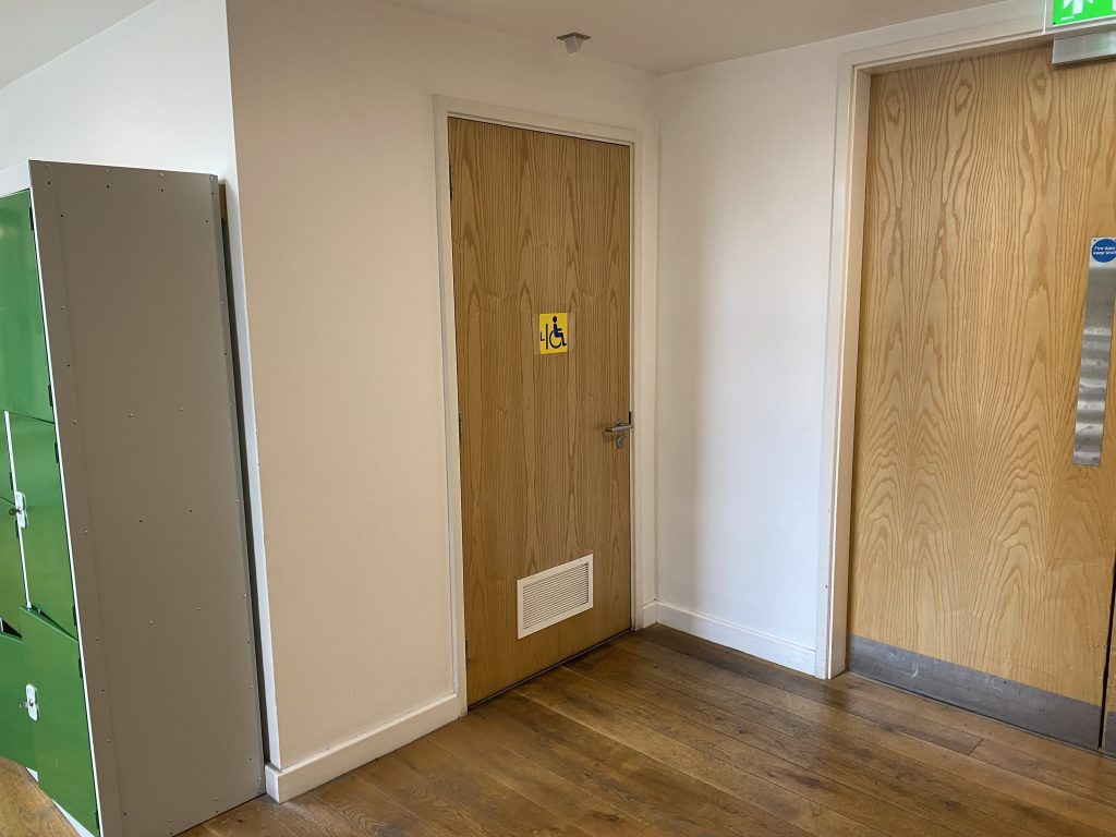 wooden door with dark blue symbol for left transfer accessible toilet on a yellow background.