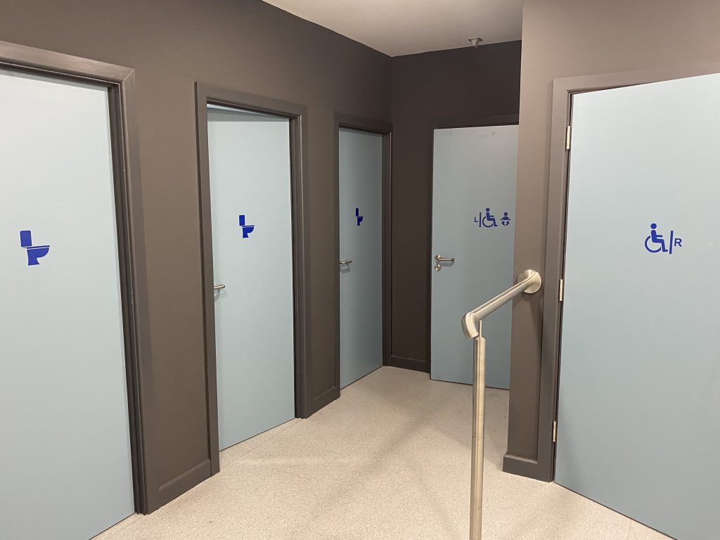 light blue doorways with dark blue symbols for gender neutral and left and right transfer accessible toilets on.