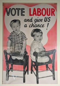 Poster with a black and white photograph of two young children sitting on chairs, with the text: 'Vote Labour and give US a chance!'.