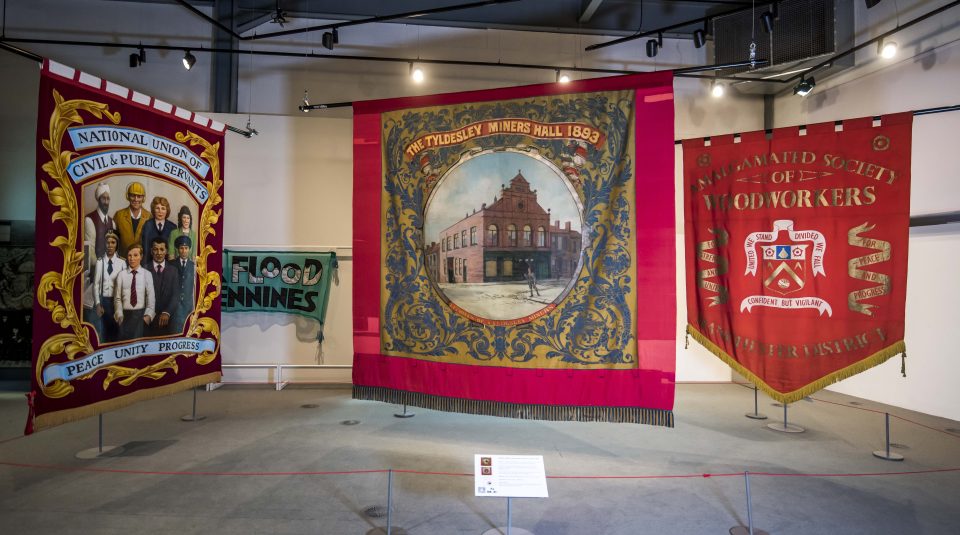 Image of Three big colourful textile banners hanging in a large gallery space.
