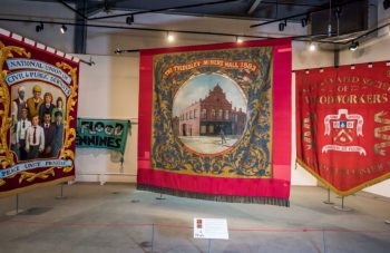 Image of Three big colourful textile banners hanging in a large gallery space.