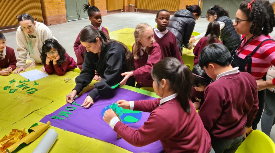 Image of Students sat at a table adding images and lettering to a purple banner