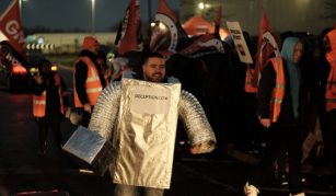 Image of Photograph showing a person in a silver robot costume with 'Deceptioncon' written on the front, and people in the background wearing orange high-vis jackets and waving GMB union flags.