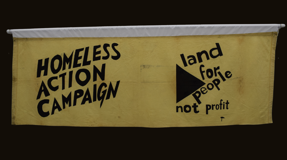 Image of Yellow landscape banner with black text: 'Homeless Action Campaign, land for people not profit'.