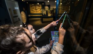 Image of Two young visitors looking up at a banner in a case, holding pencils and an activity sheet.