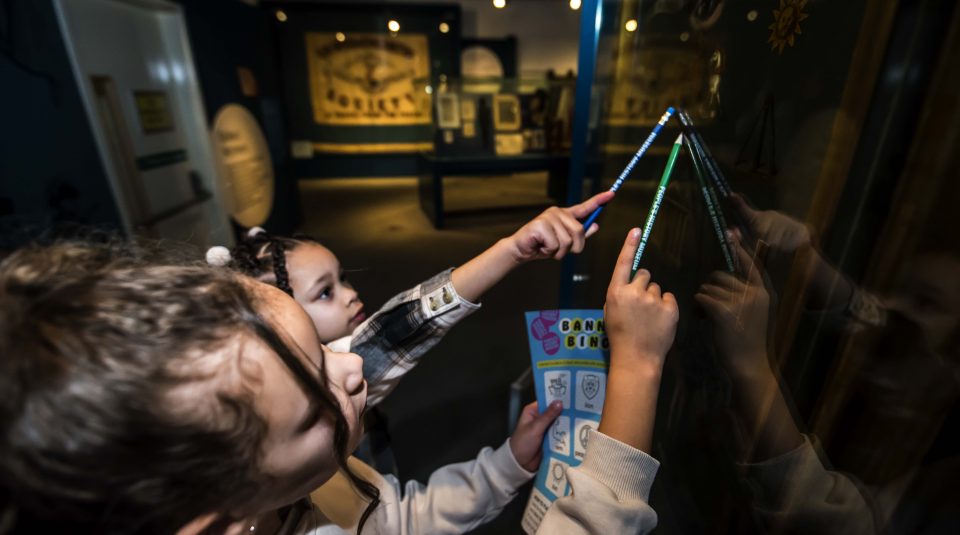 Image of Two young visitors looking up at a banner in a case, holding pencils and an activity sheet