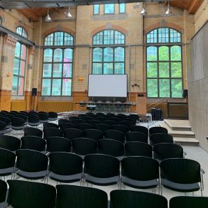 A large room with rows of chairs, a stage and a screen