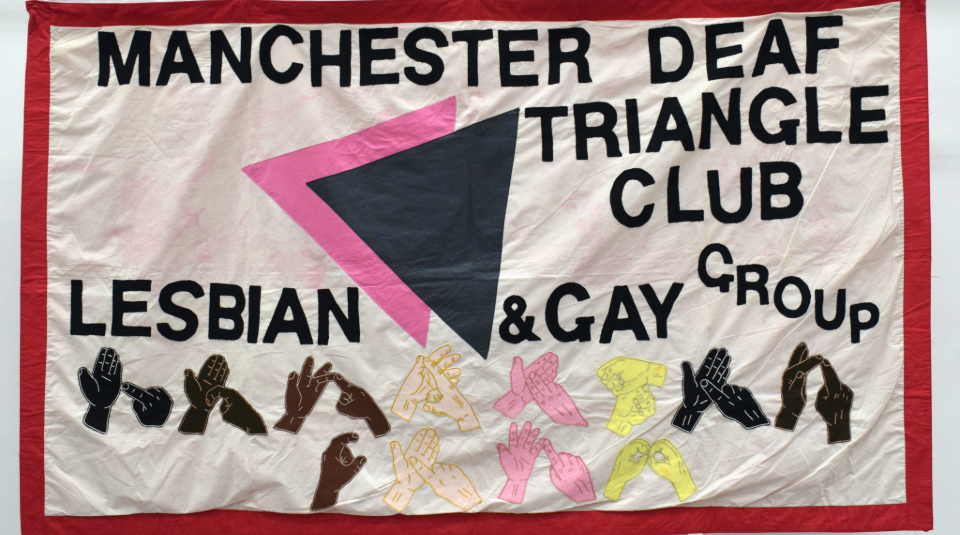 Image of A textile banner featuring text: 'Manchester Deaf Triangle Club, Lesbian & Gay Group', and different coloured hands doing sign language.