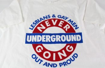 Image of white t-shirt with blue and red London Underground style logo with text: 'Lesbians & Gay Men, Never Going Underground, Out And Proud'.