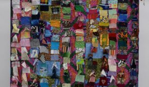 Image of A square shaped quilt made up of hundreds of small scraps of material. Each scrap has a different pattern or colour. The four corners of quilt have tassels, that have been made out of similar offcuts of material. 