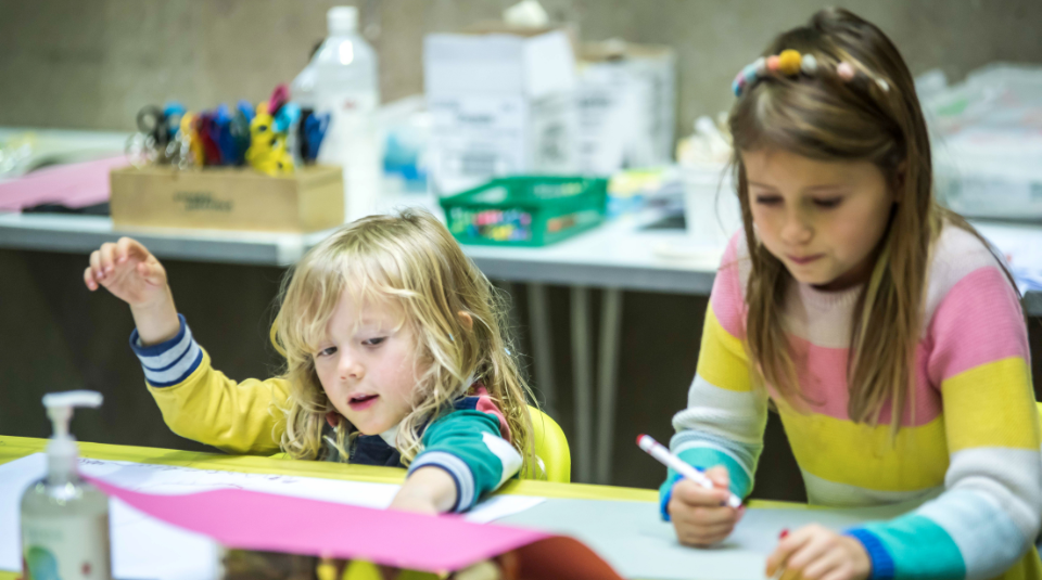 Image of Two young children wearing bright striped jumpers drawing and doing craft activities
