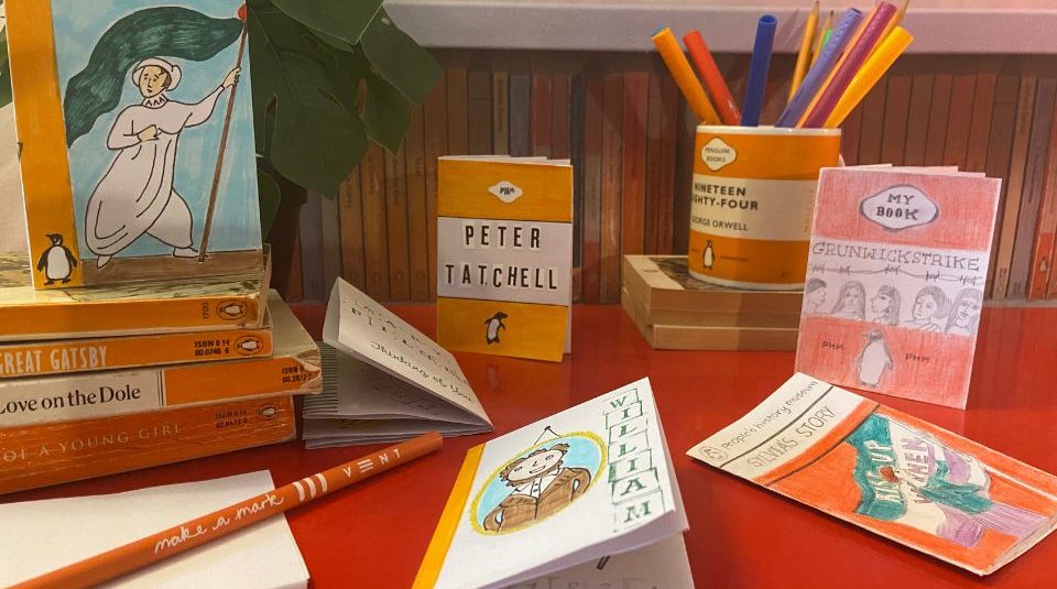 Image of Mini paper books displayed with pencils with a bookshelf behind