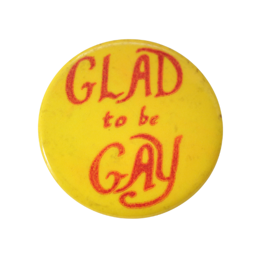 Image of Round yellow badge with hand-lettered slogan “Glad to be Gay” in red.