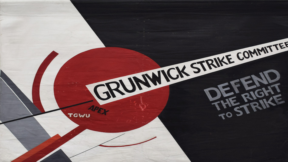 Image of A black and white banner with a geometric design which includes a large red circle, The text on the banner reads ‘GRUNWICK STRIKE COMMITTEE’ and ‘DEFEND THE RIGHT TO STRIKE,’ the acronyms 