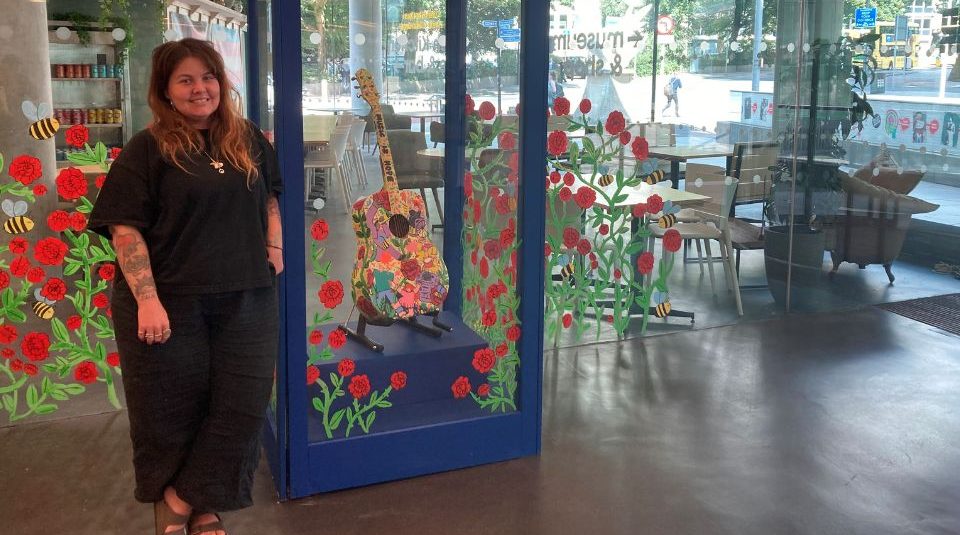 Image of A person stood next to a decorated display case containing a guitar