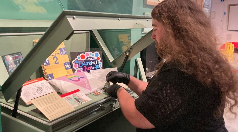 Image of Person with gloved hands adding objects to a display case