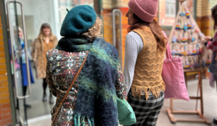 Image of 2 people wearing hats and scarves are walking out of Makers Market doors