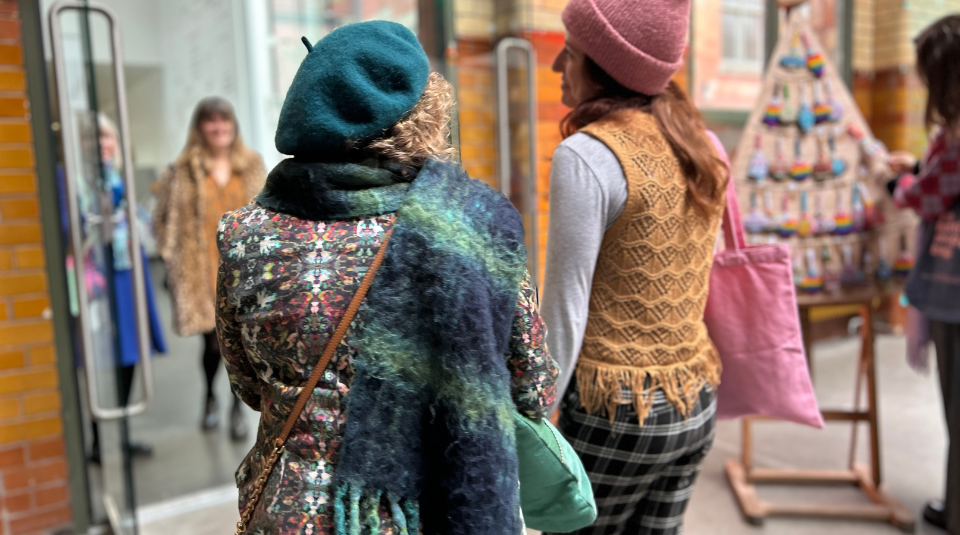 Image of 2 people wearing hats and scarves are walking out of Makers Market doors