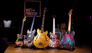 Image of A row of 5 decorated guitars standing in a line.