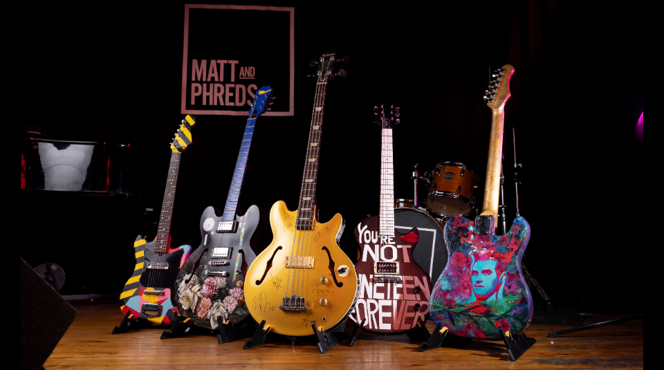 Image of A row of 5 decorated guitars standing in a line.