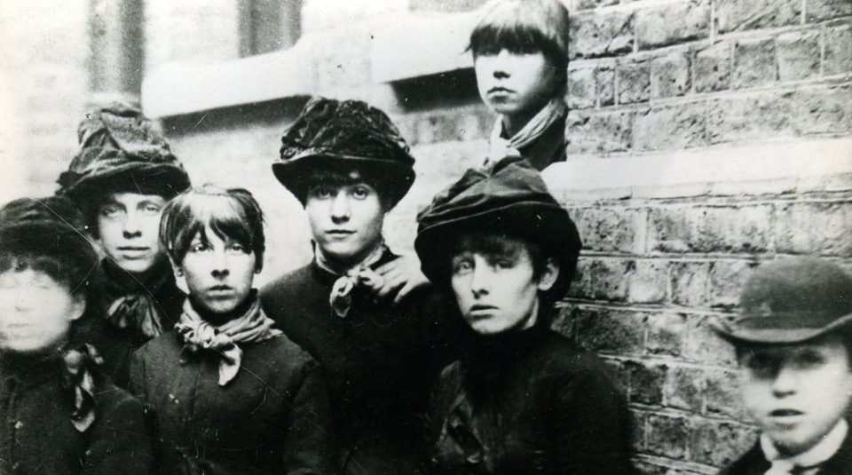 Image of Section of a black and white photo of a group of people by a brick wall.