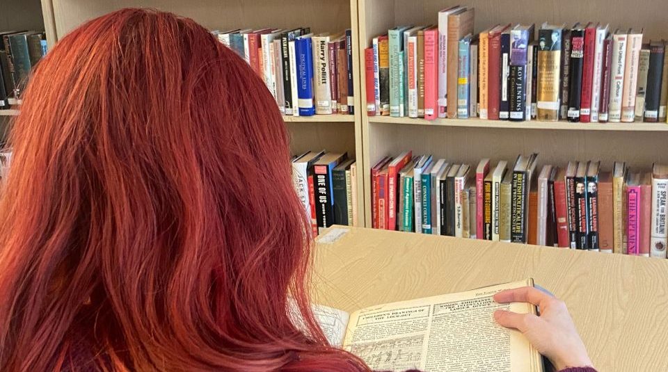 Image of A person reading archive material in front of a bookcase