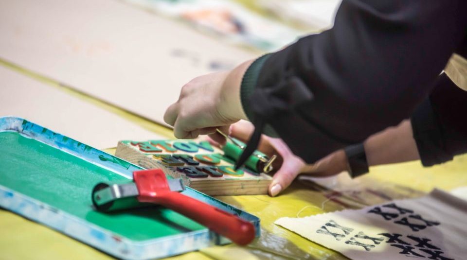 Image of A photograph showing an ink pad and a roller next to a person's hands who are using it on a stamp to print.